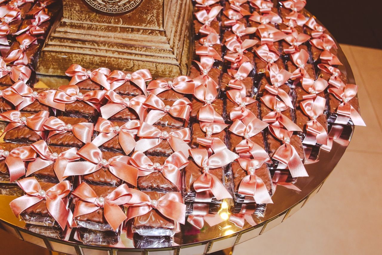 social-feed-img-01 Beautifully wrapped chocolate gifts adorned with pink ribbons arranged on a reflective table.